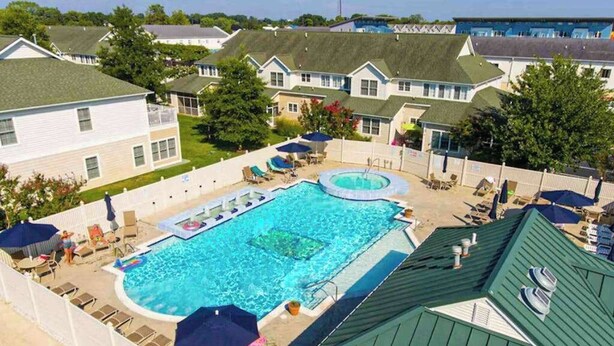 A swimming pool with lounge chairs and umbrellas, surrounded by residential-style buildings. - The Tides spacious condo w/shared pool, close to restaurants & shopping (Rehoboth Beach)