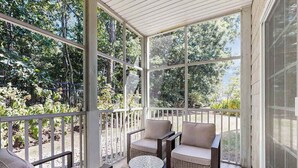 A covered porch with wicker furniture, a small round table, and a colorful rug. - The Tides spacious condo w/shared pool, close to restaurants & shopping (Rehoboth Beach)