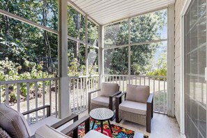 A covered porch with wicker furniture, a small round table, and a colorful rug. - The Tides spacious condo w/shared pool, close to restaurants & shopping (Rehoboth Beach)