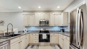 A modern kitchen with stainless steel appliances, light wood cabinets, and a granite countertop. - The Tides spacious condo w/shared pool, close to restaurants & shopping (Rehoboth Beach)