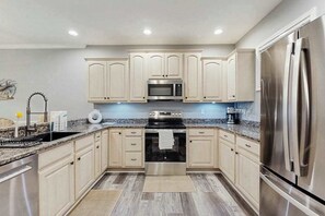 A modern kitchen with stainless steel appliances, light wood cabinets, and a granite countertop. - The Tides spacious condo w/shared pool, close to restaurants & shopping (Rehoboth Beach)
