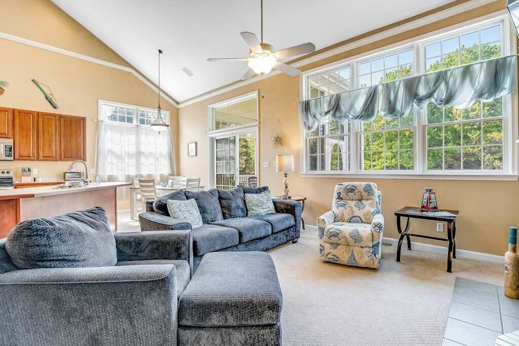A spacious living room with a sectional sofa, a patterned armchair, and a ceiling fan.