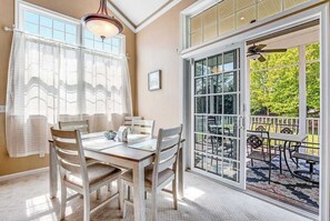 Ein Essbereich mit Tisch und Stühlen, ein großes Fenster mit Jalousien und Blick auf eine Außenpatio.