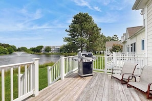 A wooden deck with a grill, chairs, and a view of a lake and buildings. - Bear Trap Dunes townhouse w/ pool, gym, free WiFi, and shared sauna (Ocean View)
