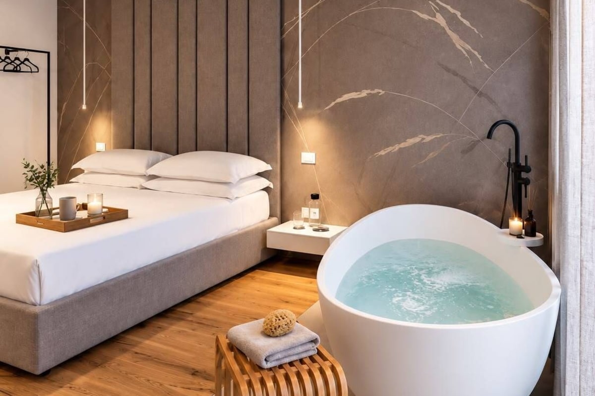 Un dormitorio moderno con una cama grande, un taburete de madera y una bañera independiente.