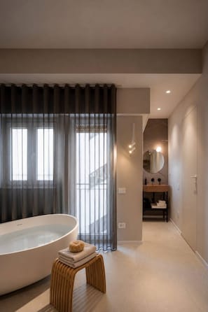 A modern bathroom with a large bathtub, a small stool, and a mirror. - Octantis (Matera)