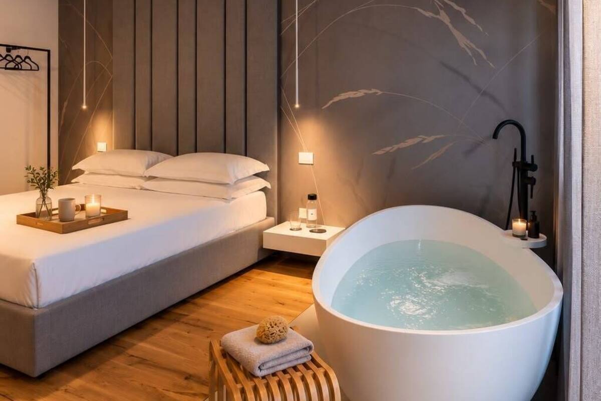 A modern bedroom with a large bed, a bathtub, and a wooden stool.