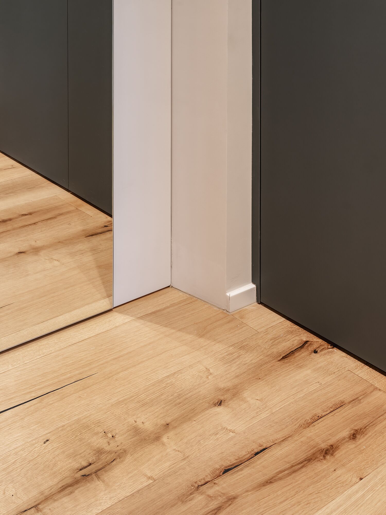Un coin de pièce avec un plancher en bois et un mur blanc.