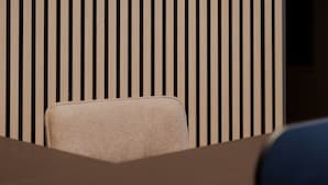 A room with a curved wall and vertical slats, a bench, and a partial view of a bed.