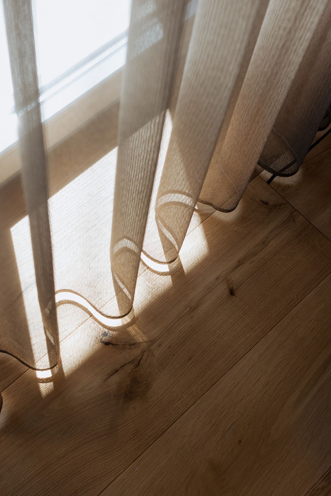 A wooden floor with a shadow cast by sheer curtains.