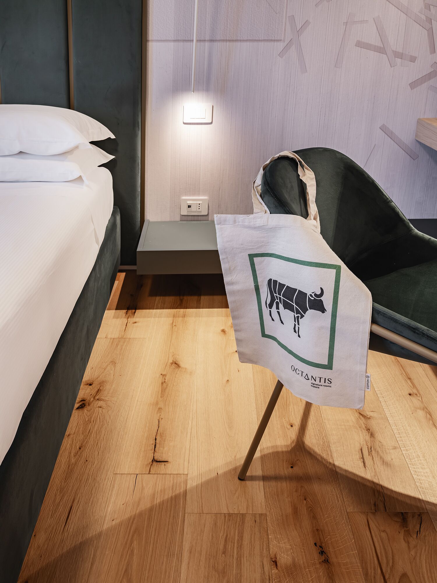 A hotel room with a bed, a chair, a nightstand, and a wall-mounted light.
