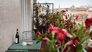 A balcony with a table, chairs, a bottle of wine, glasses, a candle, and a bowl of snacks.