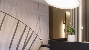 A modern hotel room with a curved wall, a black sofa, a small table, and a large pendant light. - Octantis (Matera)