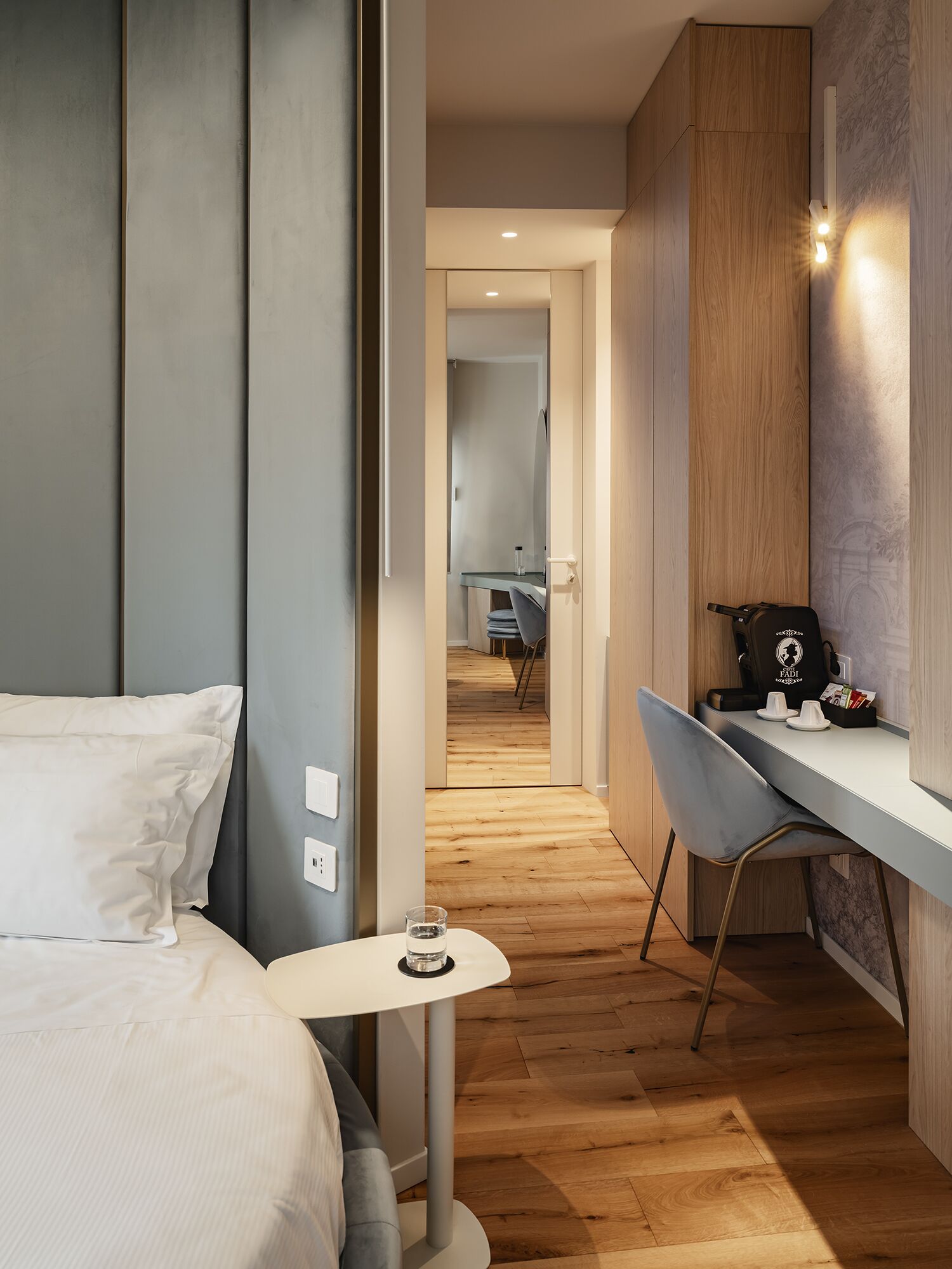 Una camera d'albergo moderna con un letto, una scrivania con una sedia, un tavolino e uno specchio.