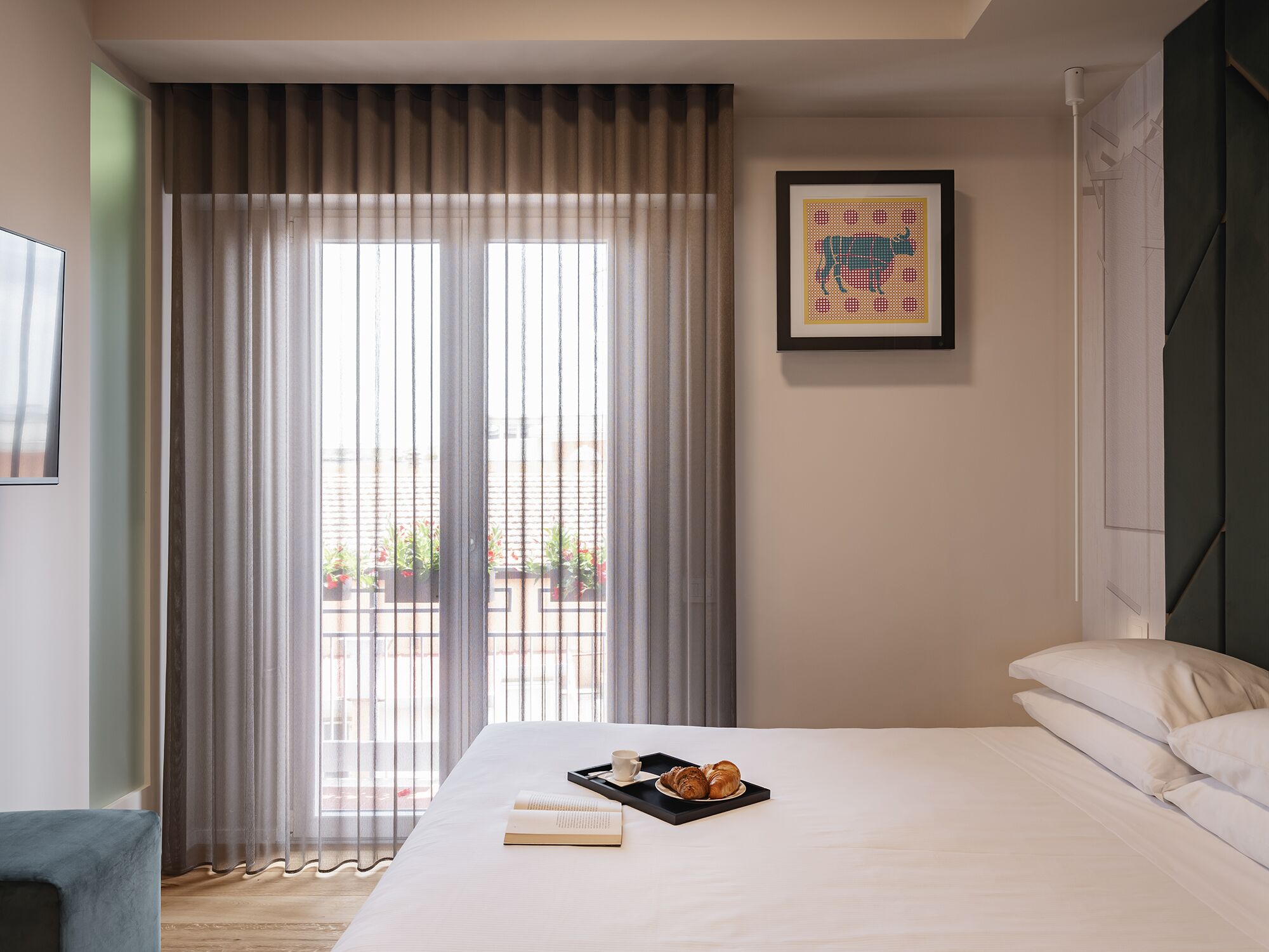 Habitación de hotel con cama, bandeja de croissants, un libro y un cuadro en la pared.
