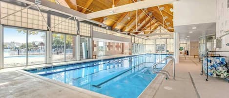 An indoor swimming pool with clear glass walls, a wooden ceiling, and a visible lifeguard station.