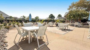 An outdoor patio area with tables and chairs, a covered seating area, and a building in the background. - Bear Trap Dunes townhouse w/ gym, pool, free WiFi, and golf on-site (Ocean View)