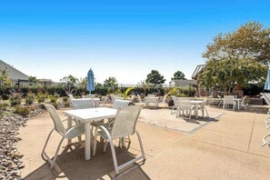 An outdoor patio area with tables and chairs, a covered seating area, and a building in the background. - Bear Trap Dunes townhouse w/ gym, pool, free WiFi, and golf on-site (Ocean View)