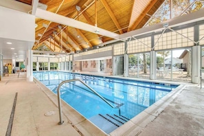 Una piscina interior con techo de madera, ventanas amplias y vistas despejadas al exterior.