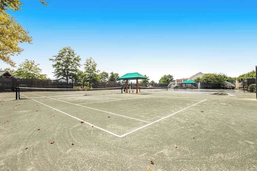 Un court de tennis en plein air, avec un filet, des parasols verts et des arbres en arrière-plan.