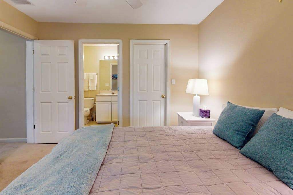 Un dormitorio con cama, mesita de noche y un baño visible a través de una puerta abierta.