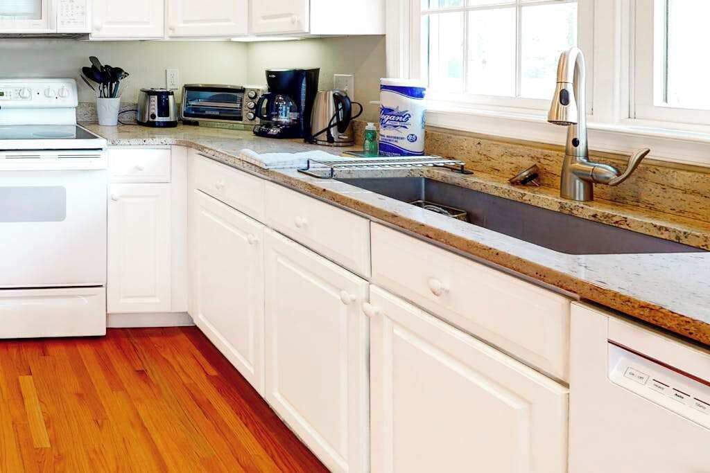 A kitchen with white cabinets, a stainless steel sink, a coffee maker, and a toaster.