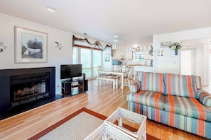 A living room with a fireplace, a television, a striped sofa, and a dining area with white furniture. - Sea Colony Tennis 1st-floor condo with tennis court, gym, & sauna (Bethany Beach)