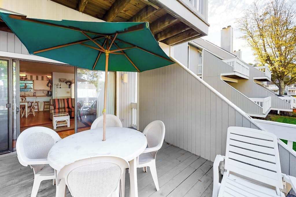 En terrasse med et bord og stole, en grøn parasol og en trappe til et højere niveau.