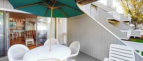 En terrasse med et bord og stole, en grøn parasol og en trappe til et højere niveau.
