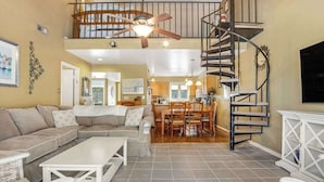 A spacious living area with a high ceiling, a dining area, and a spiral staircase. - Sea Colony tennis condo with pool, hot tub, sauna, & fitness room (Bethany Beach)