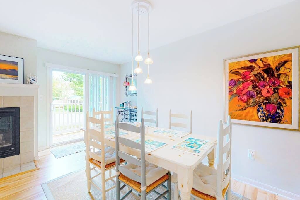 A dining area with a white table and chairs, a fireplace, and a painting on the wall.