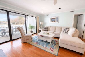 Ein Wohnzimmer mit Sofa, Sessel, Couchtisch und Blick durch eine Glastür.