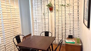 Un coin repas avec une table et des chaises en bois, un luminaire suspendu, une plante en pot et une petite table sur laquelle se trouvent un livre et une bouteille verte.
