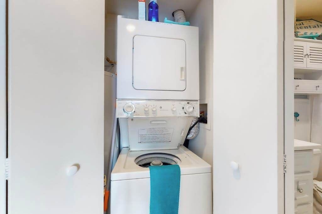 Uma área de lavanderia compacta com máquina de lavar e secadora empilhadas, uma toalha azul-turquesa e um armário branco com uma placa.