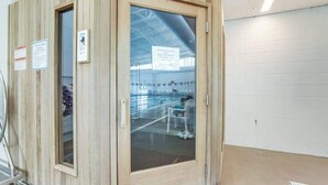 A wooden door with a glass panel, a metal cart, and a tiled wall. - 1st-floor Sea Colony Tennis condo with pool, gym, & fireplace (Bethany Beach)