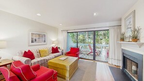 A living room with a sofa, armchairs, a coffee table, a fireplace, and a large sliding glass door leading to an outdoor area. - 1st-floor Sea Colony Tennis condo with pool, gym, & fireplace (Bethany Beach)