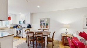 Una cocina moderna con muebles blancos, un microondas y un comedor con mesa y sillas de madera.