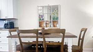 A dining area with a wooden table and chairs, a window with potted plants, and a white cabinet with a coffee maker. - 1st-floor Sea Colony Tennis condo with pool, gym, & fireplace (Bethany Beach)