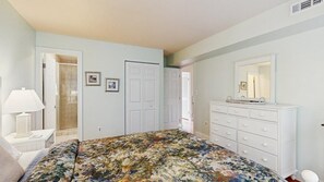 Une chambre à coucher comprenant un lit, une commode, un miroir et une porte donnant sur une autre pièce.