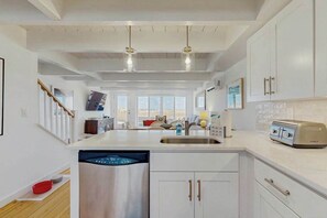 Una cocina moderna con muebles blancos, lavavajillas, tostadora y vista al área de estar.
