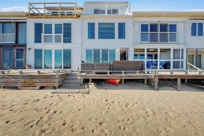 Una propiedad frente a la playa con un edificio de varios pisos, una terraza de madera y una playa arenosa.