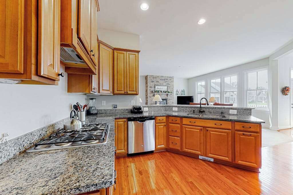 A modern kitchen with granite countertops, wooden cabinets, a stainless steel dishwasher, and a large window offering a view of the city.