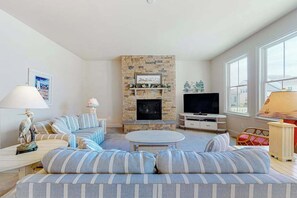 A living room with a stone fireplace, a television, striped sofas, and a lamp. - Beautiful home close to beach with pool, tennis, washer/dryer, WiFi, AC (Rehoboth Beach)