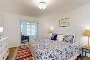 Ein Schlafzimmer mit einem Bett, einem Nachttisch, einer Lampe, einem Fenster und einer Tür zu einem anderen Raum.