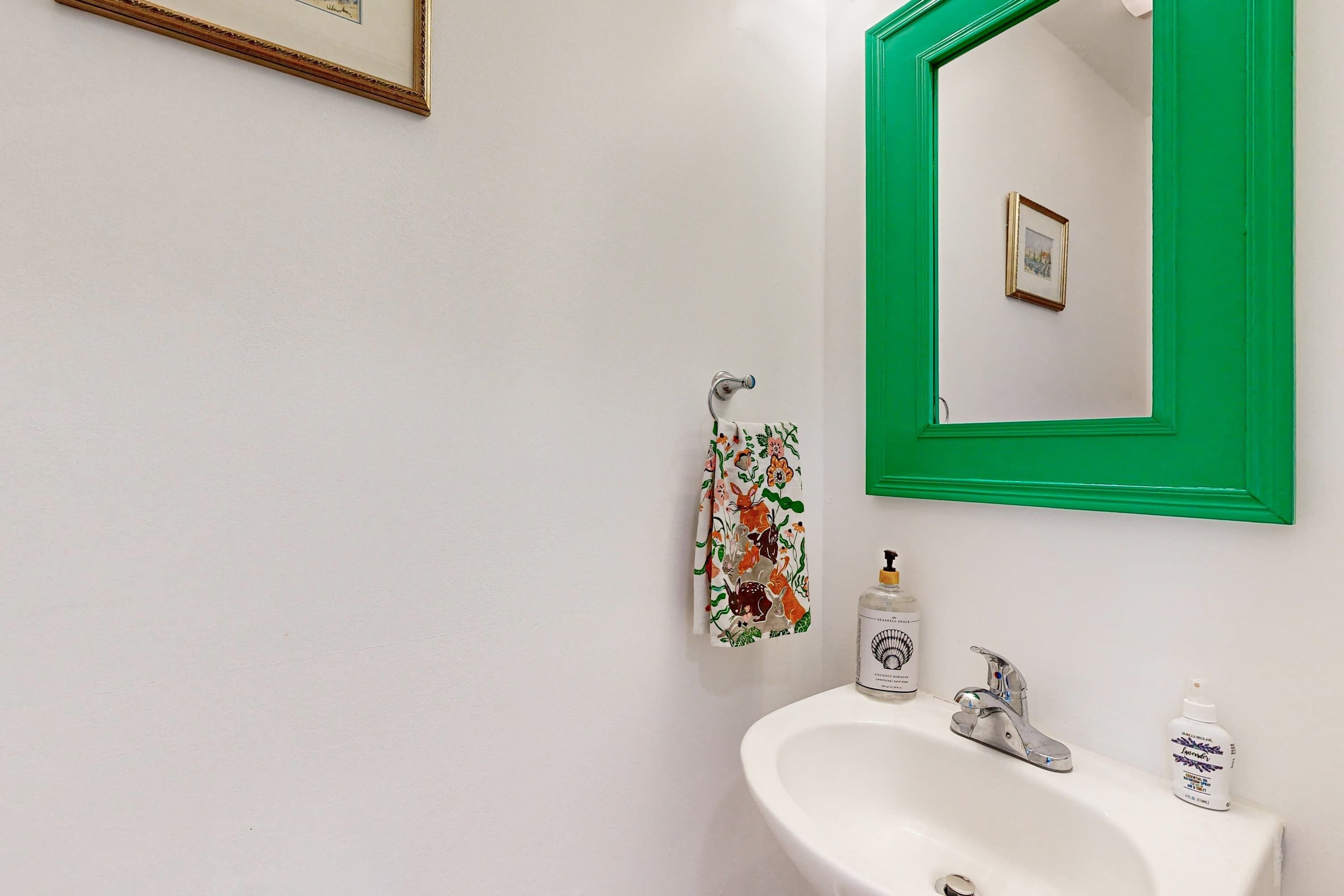 A bathroom with a white sink, green-framed mirror, and a towel with a deer pattern.