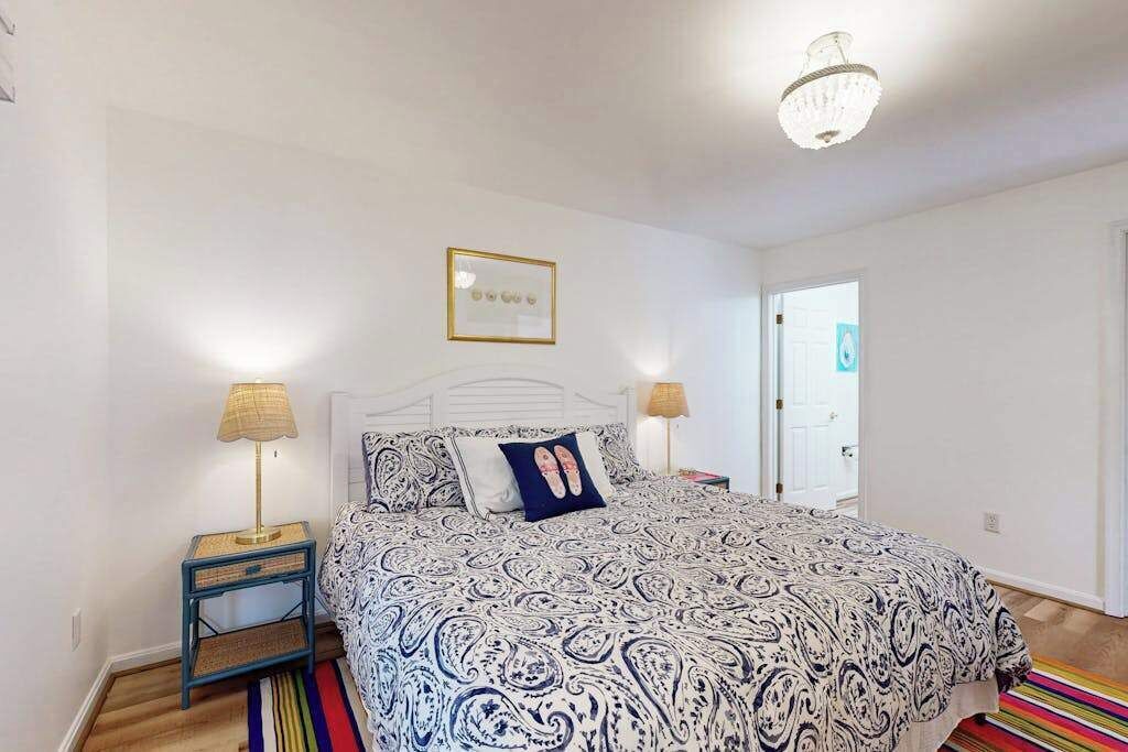 A bedroom with a patterned bedspread, two bedside lamps, a framed picture on the wall, and a striped rug.