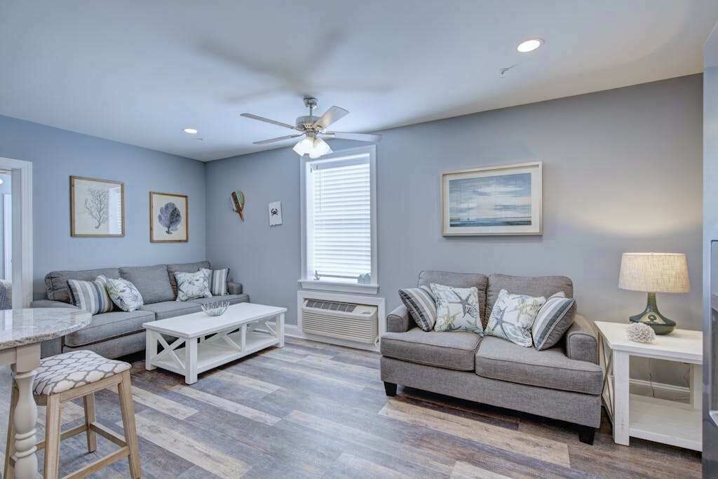 A living room with a grey sofa, a white coffee table, a ceiling fan, and a window with blinds.