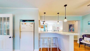 A kitchen with a white refrigerator, bar stools, pendant lights, and a door with frosted glass panels. - Town of Rehoboth Beach home in a great location with yard and 3-season room (Rehoboth Beach)