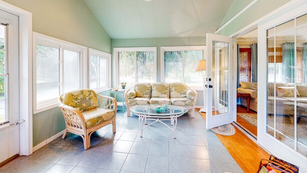 A sunlit room with a sofa, armchair, and coffee table, large windows, and a sliding glass door leading to another room. - Town of Rehoboth Beach home in a great location with yard and 3-season room (Rehoboth Beach)