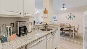 A kitchen with white cabinets, a coffee maker, a sink, and a dining area with a table and chairs. - Villas at Bay Crossing - perfectly appointed with pool & patio - beaches nearby (Lewes)